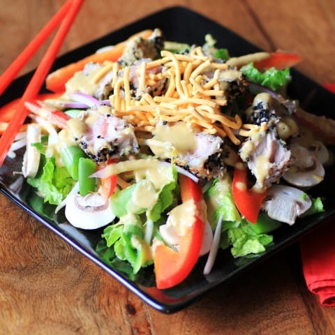 This Ahi Tuna Salad will fill the void for an Asian craving. Gorgeous slightly seared crusted tuna is on top of a bed of salad with the best Asian dressing around! Finish it off with a little crunch from some chow mein noodles and you have the perfect salad. Ahi Tuna Salad on a black plate with chop sticks
