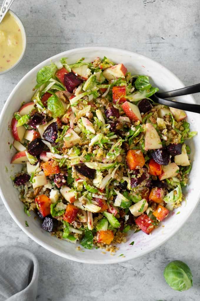 A fall harvest salad that celebrates all things fall. Loaded with brussels sprouts, blue cheese, crispy quinoa, roasted beets, and butternut squash and topped with the most delicious champagne apple cider vinaigrette! #fallsalad #harvest #applevinaigrette Fall Harvest Salad in a white bowl