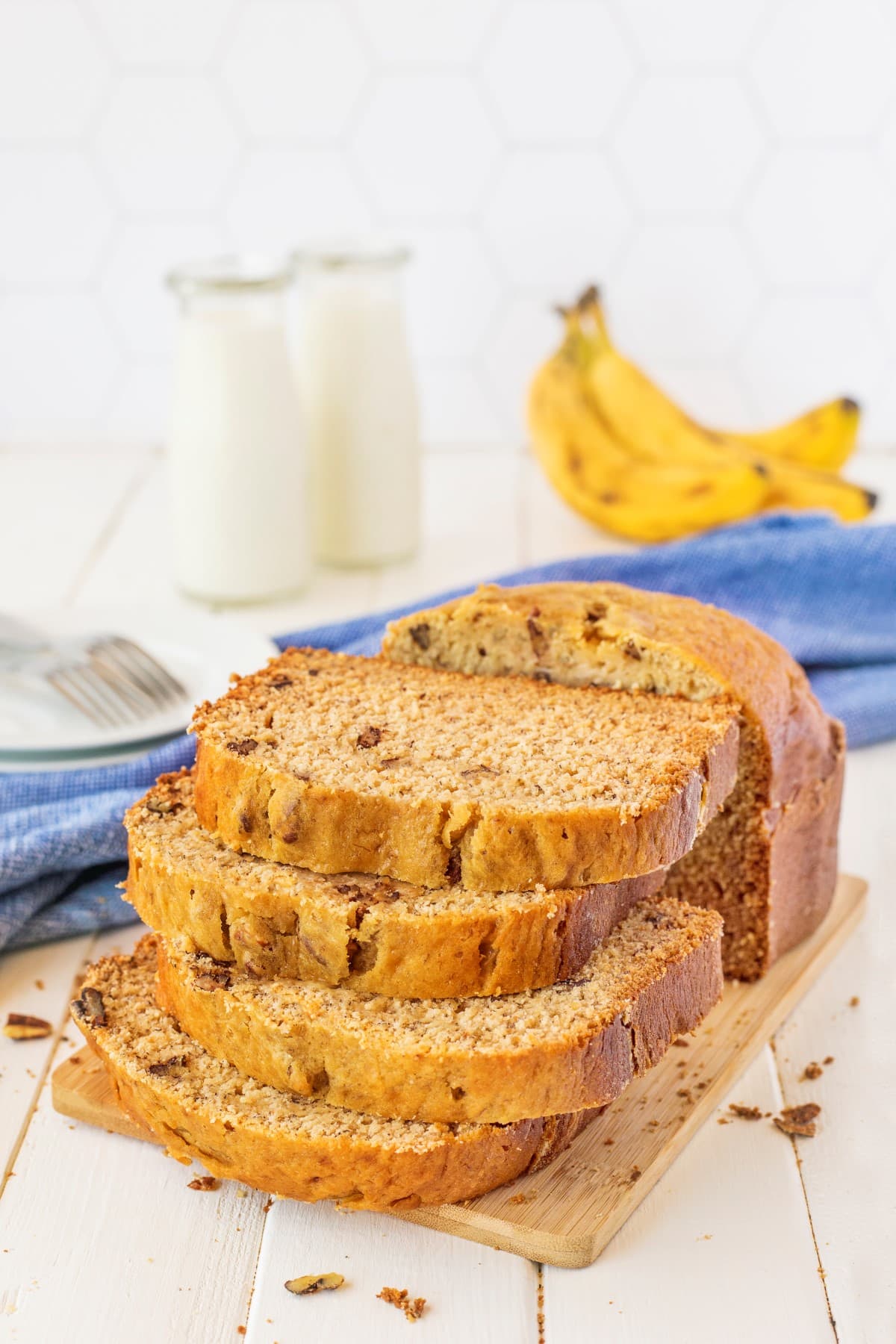 The Super Easy Bread Machine Banana Bread is a dump-and-go recipe and, in a matter of hours, will fill your home with the fresh smell of bread baking. Stacked banana bread on a wooden board with milk and bananas in the background.