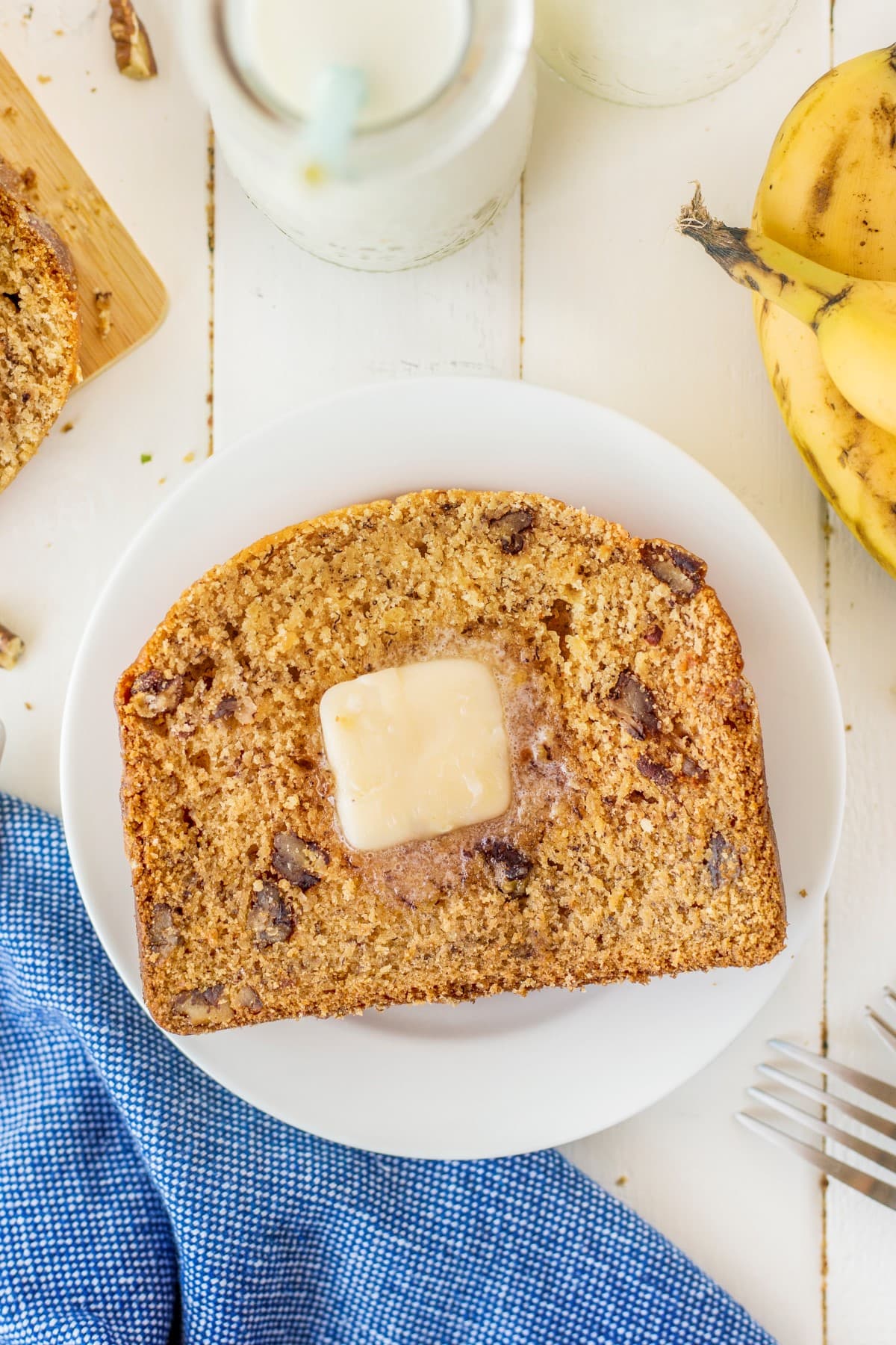 The Super Easy Bread Machine Banana Bread is a dump-and-go recipe and, in a matter of hours, will fill your home with the fresh smell of bread baking. Banana bread on a white plate with a pat of butter.