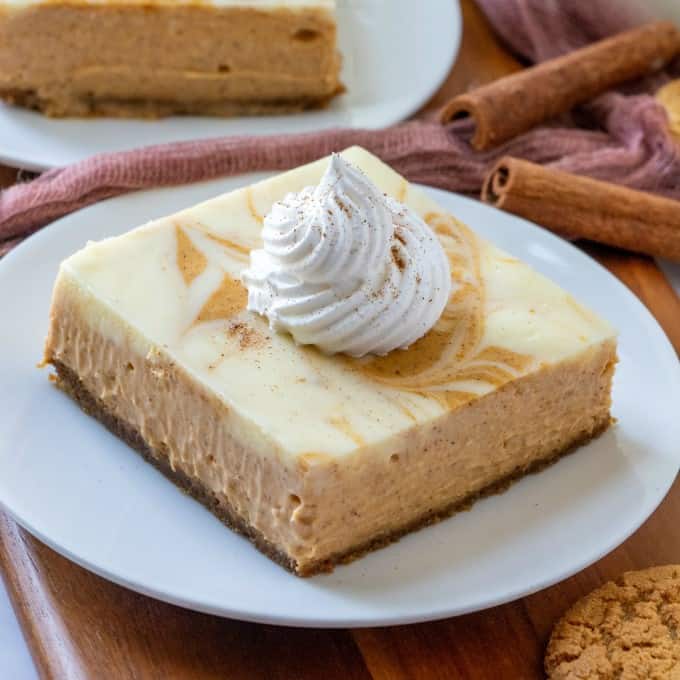 These Easy Swirl Pumpkin Cheesecake Bars are simple to make and a great make ahead dessert! Perfect for Thanksgiving!! Closeup of pumpkin cheesecake bars with whipped cream on top.