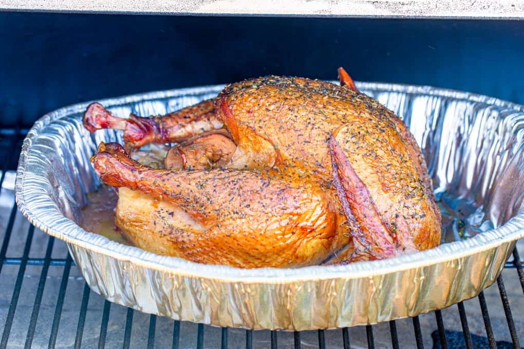 The Quintessential Guide for Smoking a Turkey will help you through brining, smoking and the best gravy ever! You won't find a better turkey than this. Turkey in a roasting pan in a smoker
