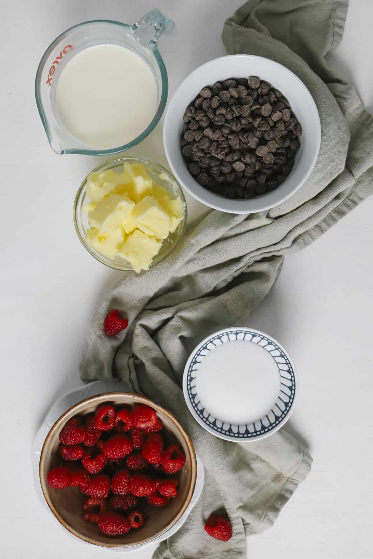 This delicious, decadent chocolate tart is a perfectly balanced recipe with a rich chocolate ganache and a raspberry jam on a buttery crust. Top view of ingredients in small ramekins with a grey towel
