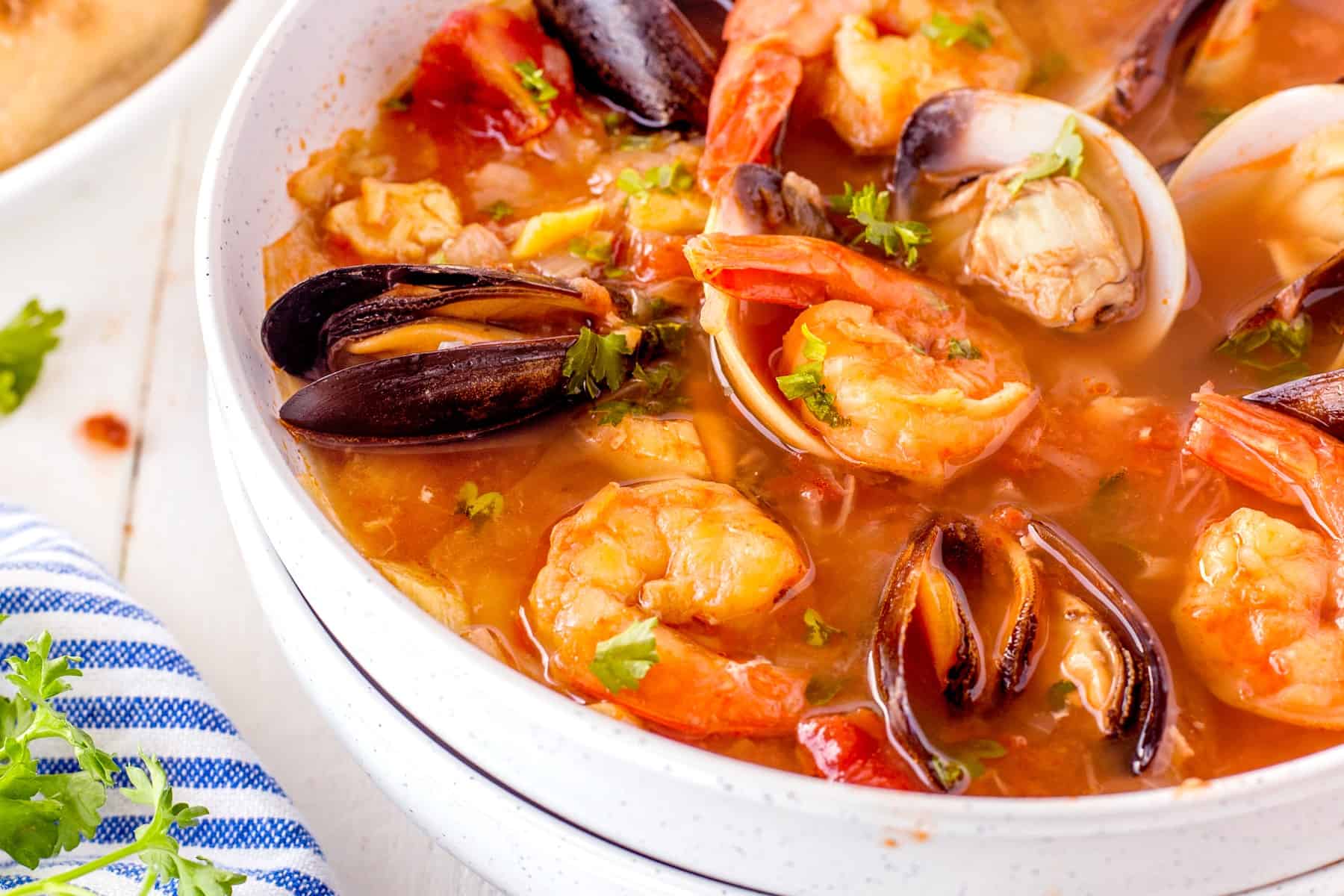 Cioppino (Fisherman's stew) is filled with shrimp, clams, mussels, white fish, and snow crab claws and simmered in a rich broth made from tomato/garlic and fish stock. Horizontal pictures of seafood stew.