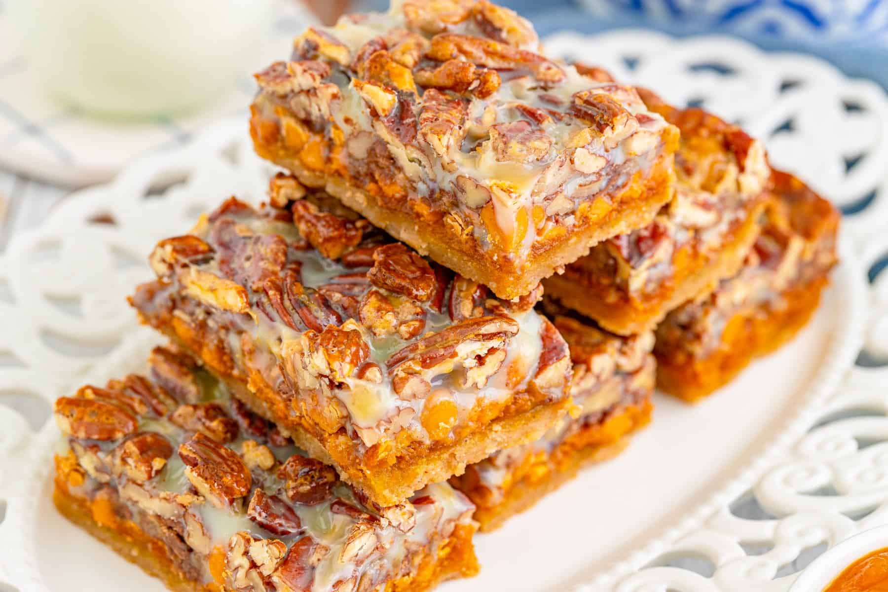 These Pecan Magic Pumpkin Bars are irresistible for a fall treat. Layers of cookie bottom, pumpkin, butterscotch, toffee and more make for a great fall treat. Horizontal platter with pumpkin bars stacked on it,