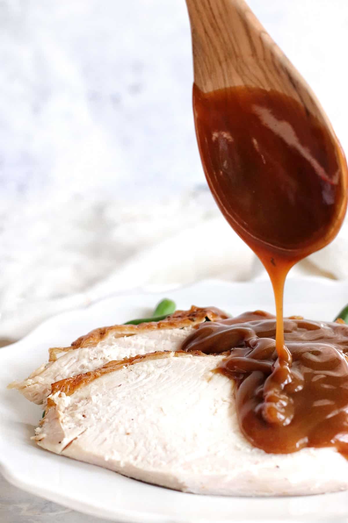 Air Fryer Turkey Breast is an amazing way to enjoy this moist and tender meat for Thanksgiving, Christmas or any Sunday Supper. Pouring rich brown gravy from a wooden spoon onto sliced air fryer turkey breast.