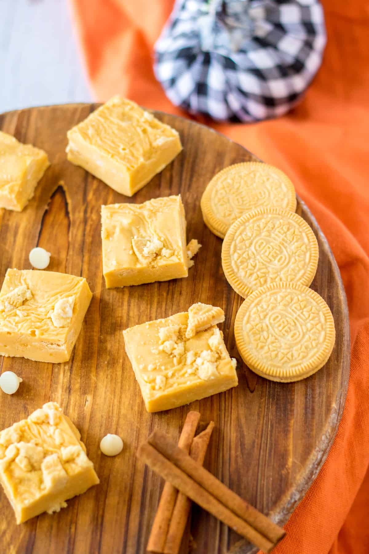 Easy Oreo Pumpkin Pie Fudge is a classic candy treat for fall with a twist of added vanilla Oreo cookies. Make this for Thanksgiving or for any fall day. Easy Oreo Pumpkin Pie Fudge on a wooden board with cinnamon and vanilla Oreo cookies.