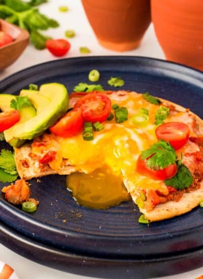 Showing a runny egg yolk coming off of a Sheet Pan Huevos Rancheros on a blue plate.