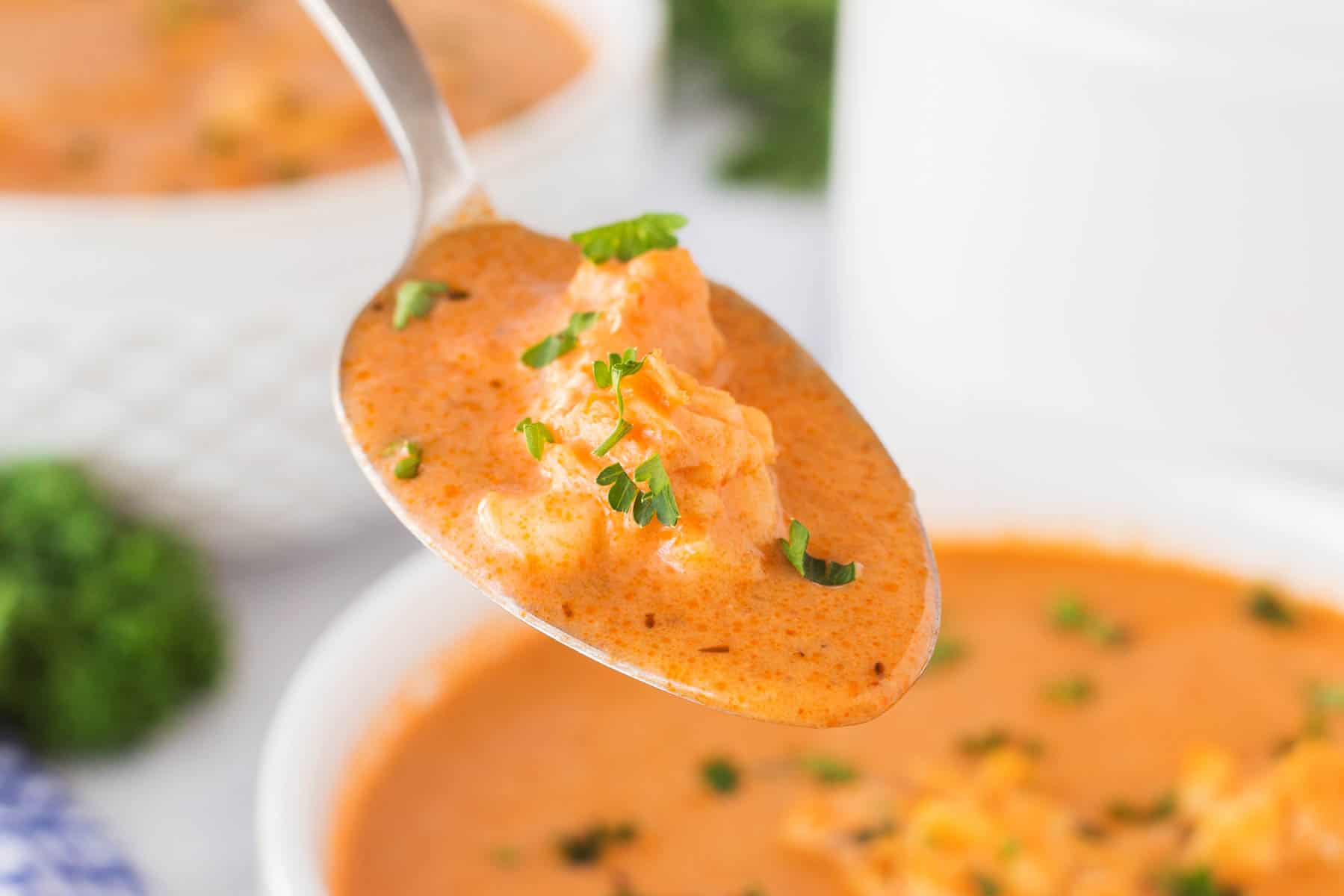 This Best Lobster Bisque Recipe is a tried and true recipe that is bursting with flavor and chunks of wonderful lobster in each bite. Horizontal close-up of a spoonful of lobster bisque.