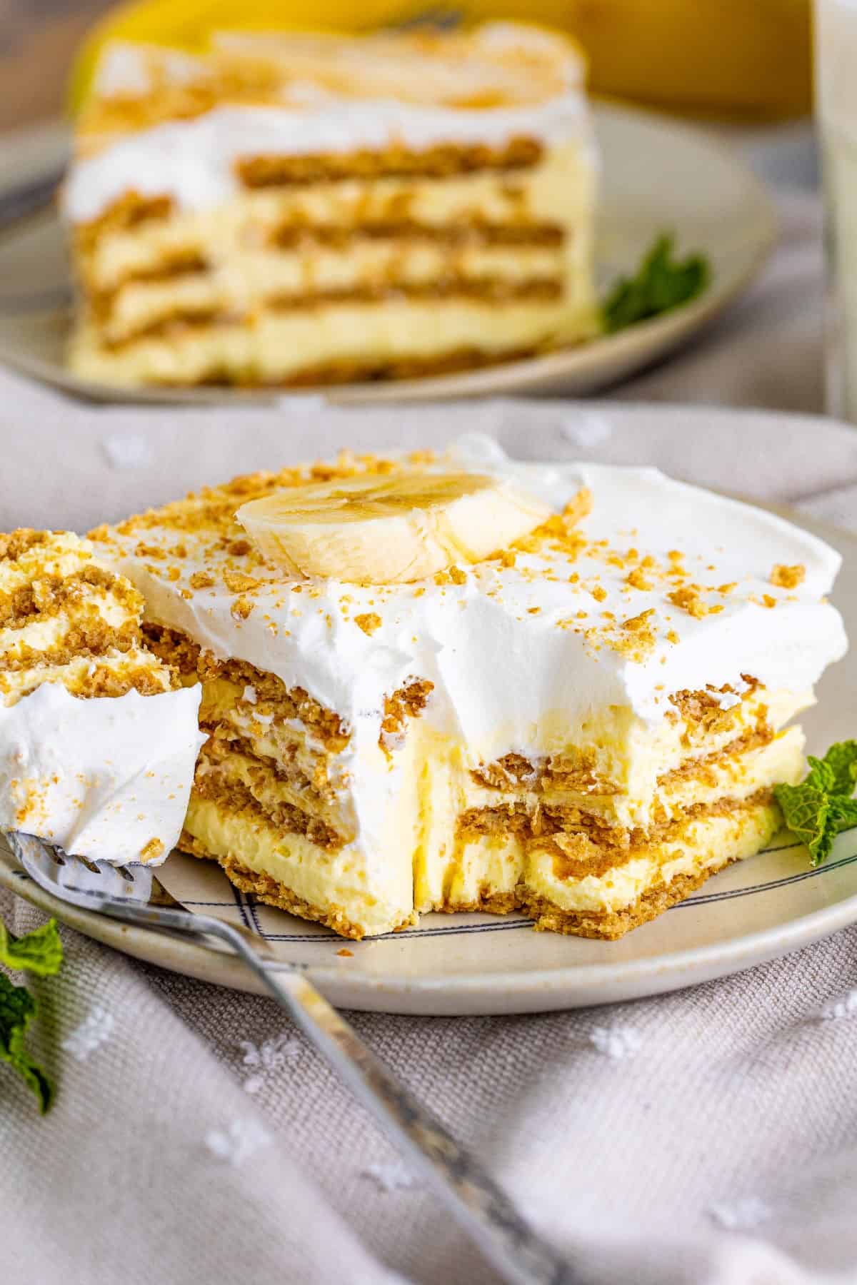 This Banana Icebox Cake is like an amazing banana cream pie but without all the fuss. So easy to make and always a winner at any gathering. A serving of Banana Icebox Cake on a plate with a forkful on the side.