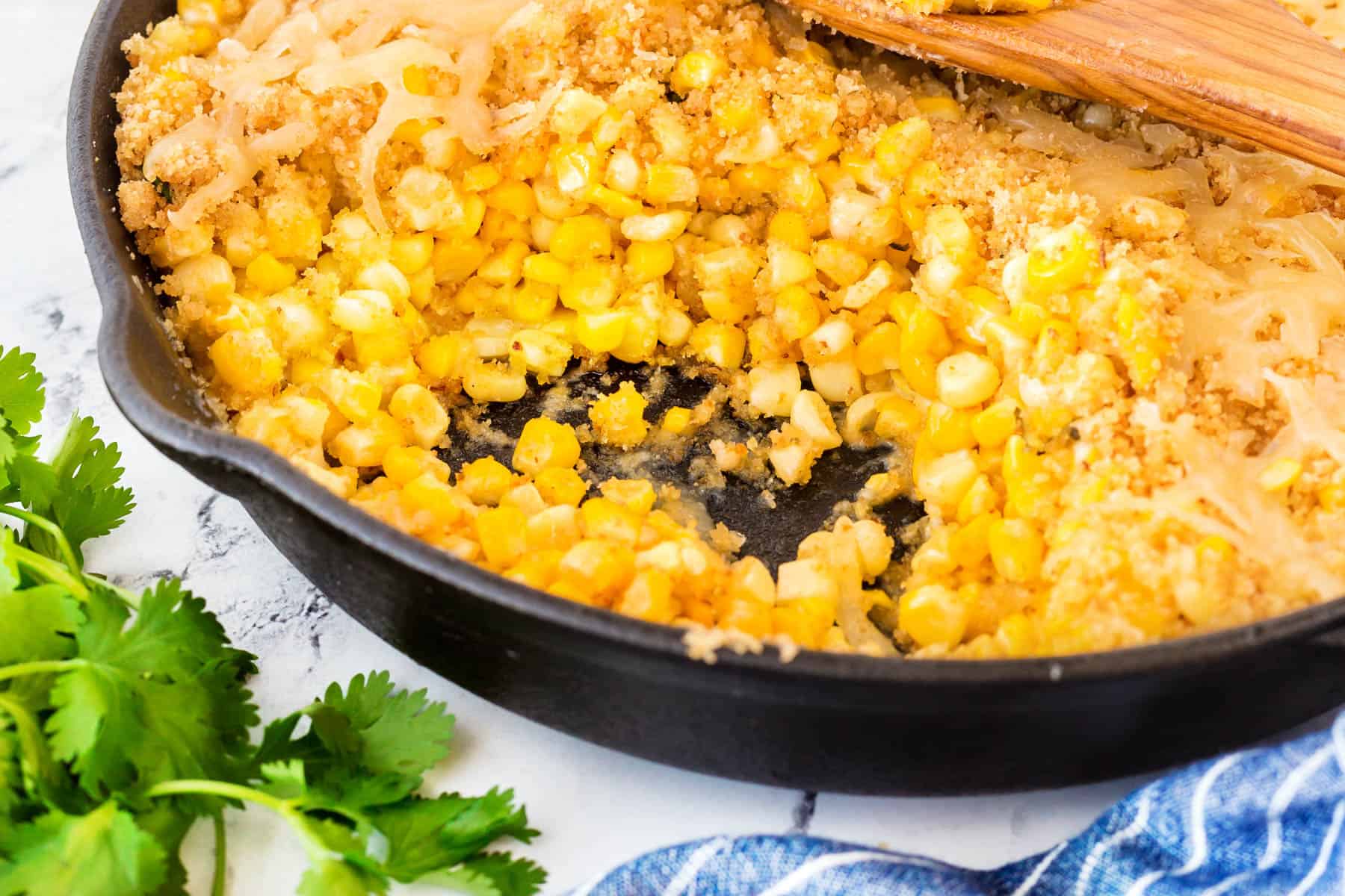 This Easy Cheesy Skillet Corn recipe is fantastic with fresh corn in the summer but equally as good using frozen corn for the holidays. Horizontal shot of skillet corn in a cast iron pan.