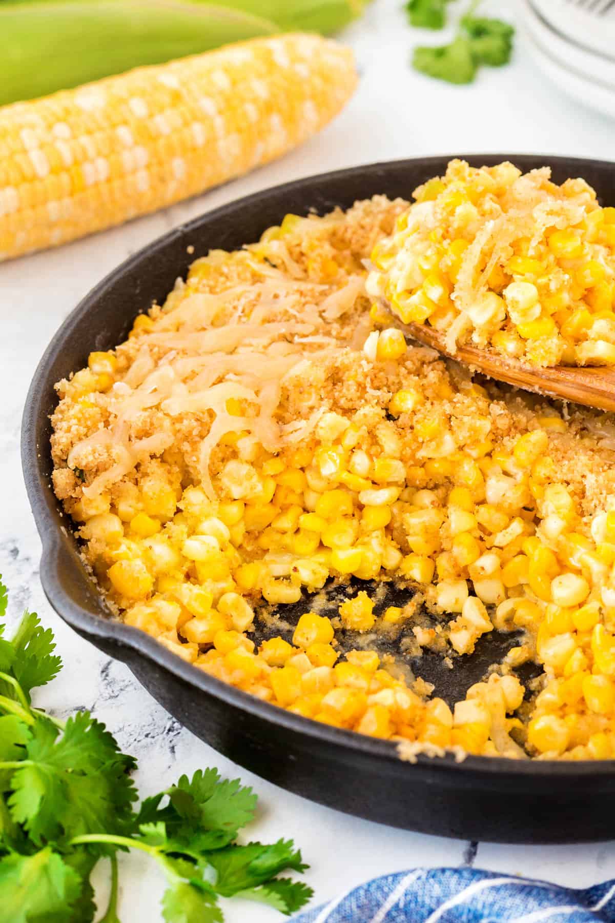 This Easy Cheesy Skillet Corn recipe is fantastic with fresh corn in the summer but equally as good using frozen corn for the holidays. Easy Cheesy Skillet Corn in a cast iron pan with a scoop taken and resting on top.