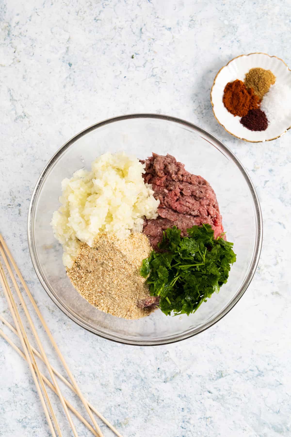 Transparent bowl with ground lamb, parsley, chopped onion and crumbs.