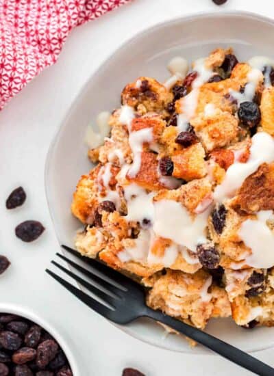 Slight overhead shot of bread pudding with sauce on a plate with a black fork.
