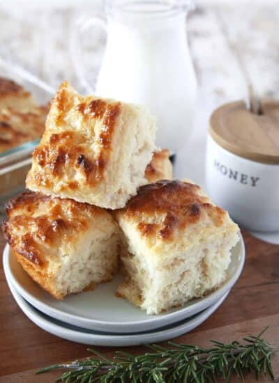 Butter Swim Biscuits piled high on a plate. Honey in the background and rosemary sprigs in the foreground.
