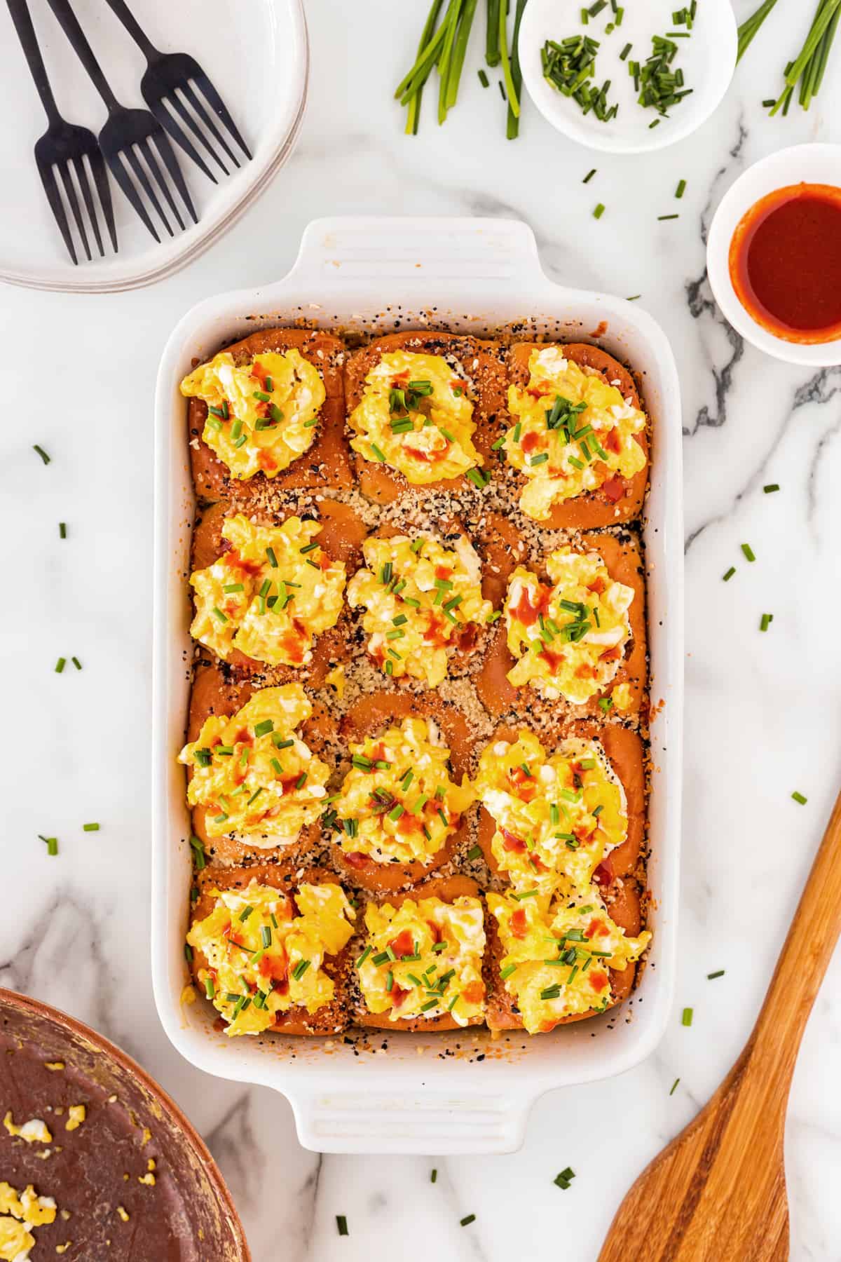 These Stuffed Bacon Egg Breakfast Sliders are the perfect holiday or Sunday brunch menu item. They are a complete breakfast all-in-one sandwich and will easily feed a crowd. White casserole dish filled with bacon, egg, and cheese sliders garnished with chopped chives.