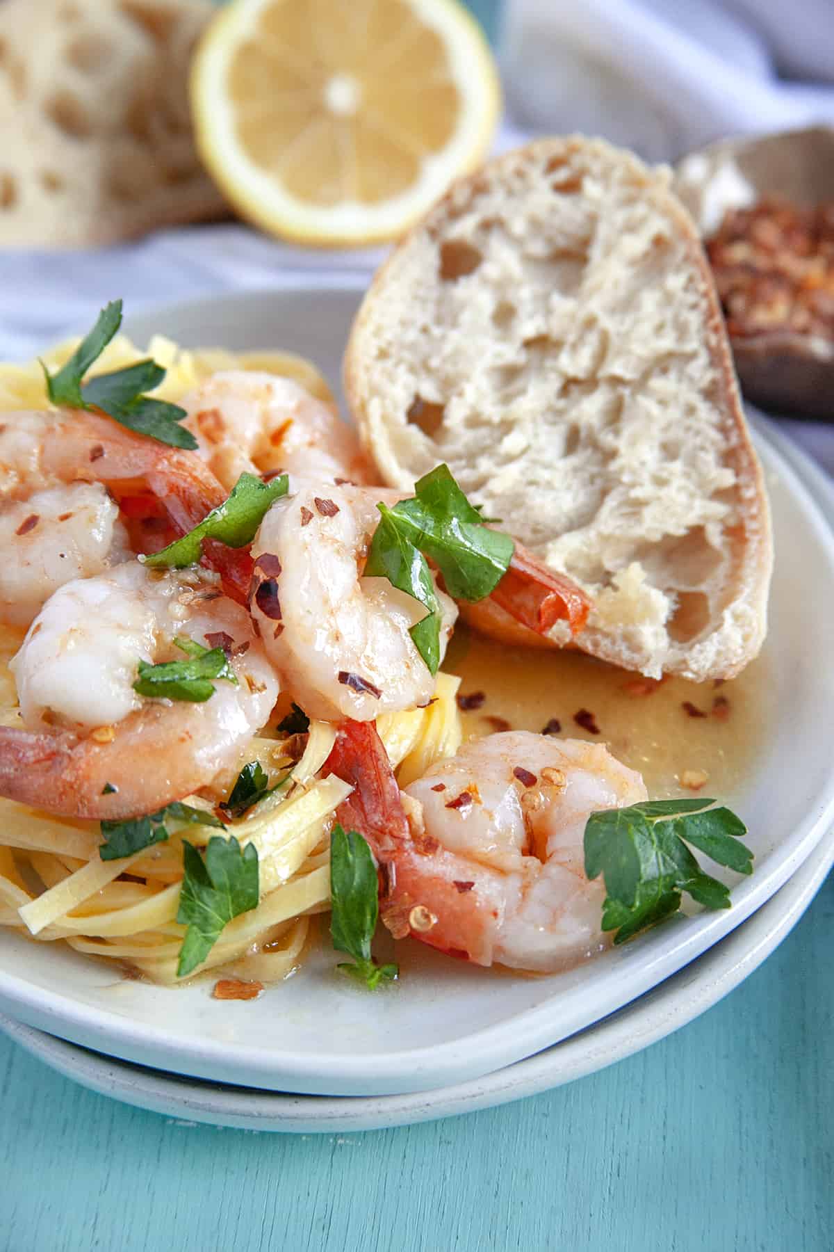 This Shrimp Scampi is a delicious dish to share for Valentine's Day or an anniversary. The succulent garlic butter shrimp are always a hit. Vertical shot of shrimp scampi over pasta with crusty bread.