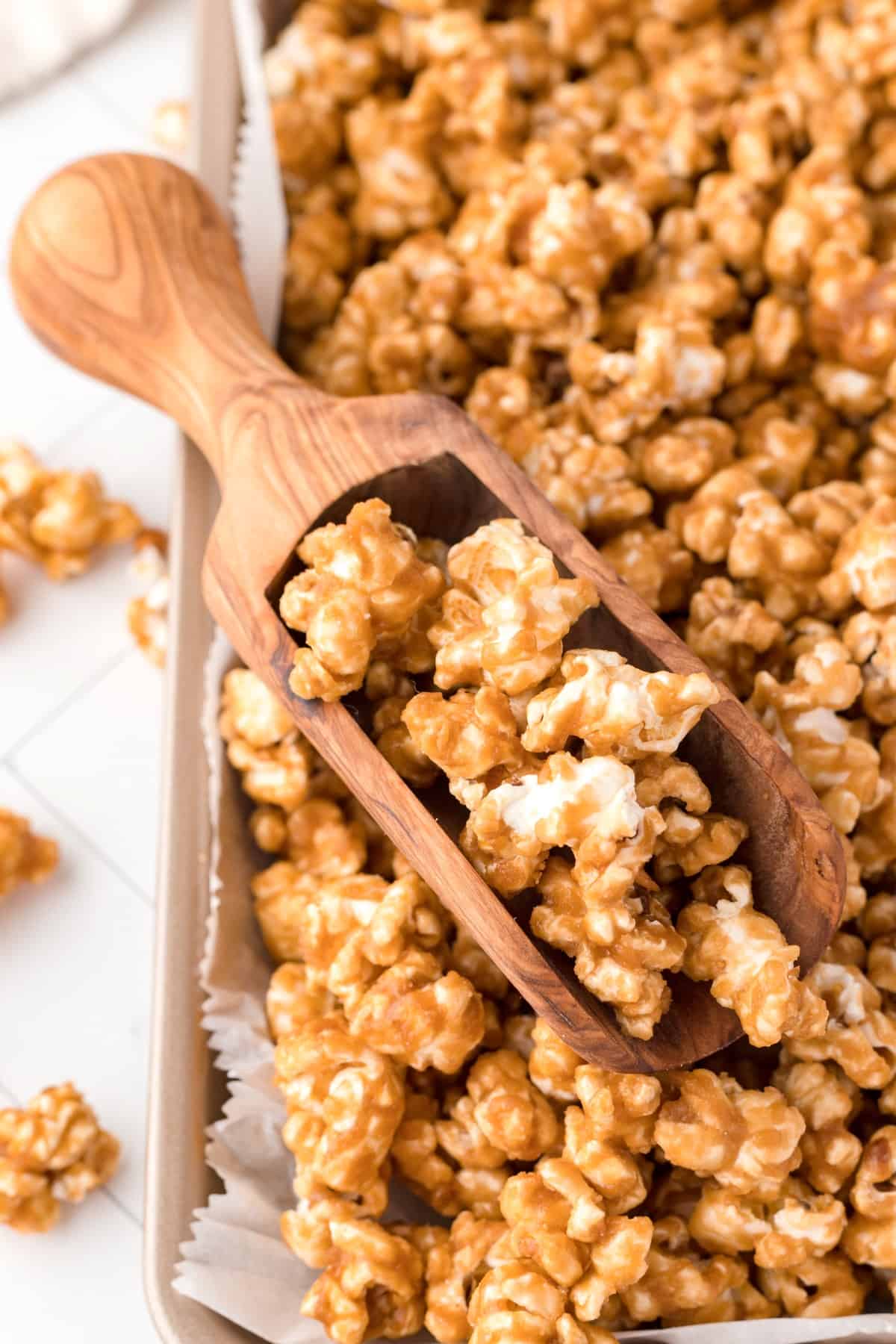 Crunchy, buttery, sweet and satisfying, Caramel Corn has it all. This nostalgic candy treat is loved by young and old and is an easy treat to make up for any occasion. Close-up shot of caramel corn on a baking sheet with a small wooden scoop.