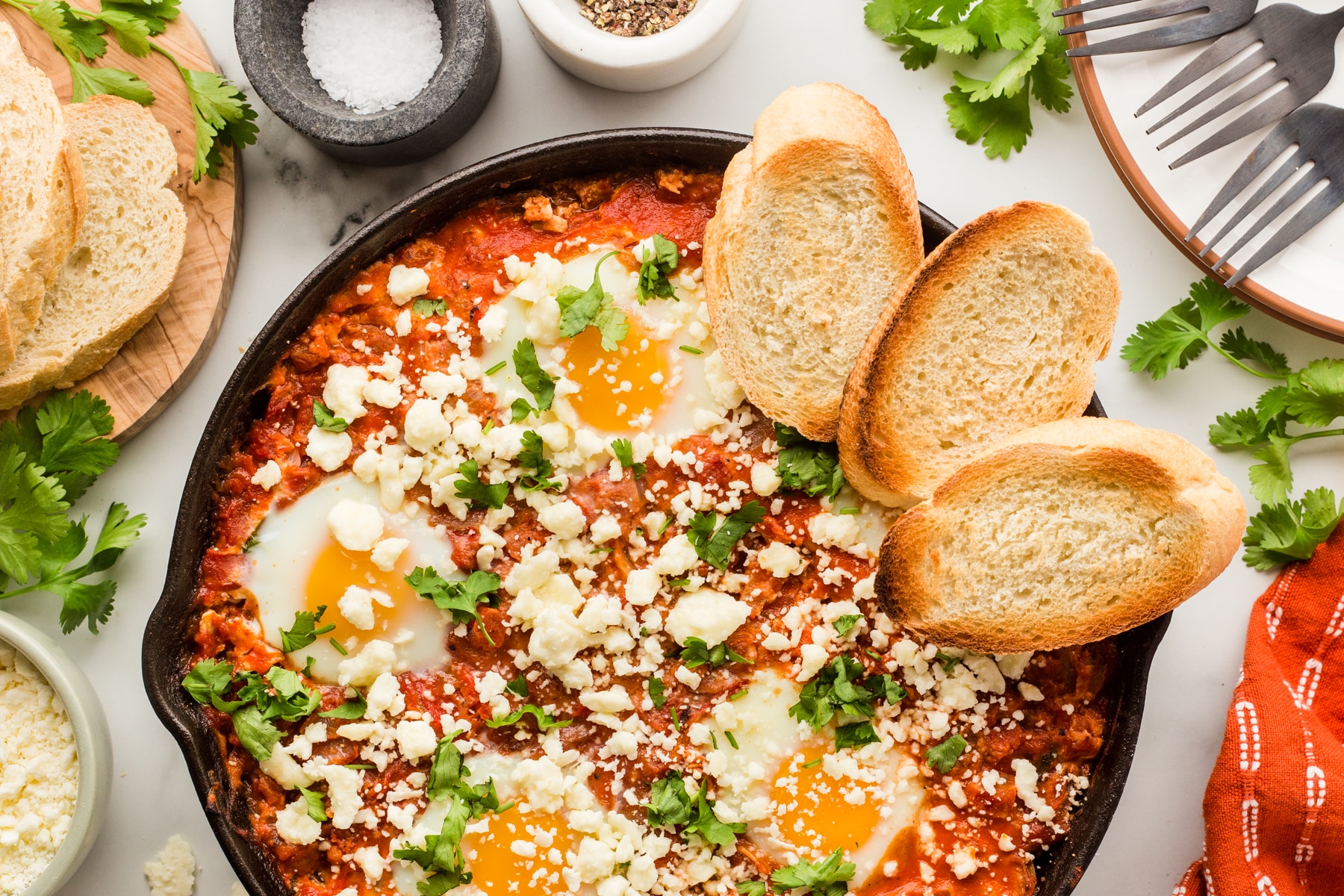 The Shakshuka Recipe is the best. Bursting with flavors, you will never believe that these simple ingredients can have so much flavor. Perfect for breakfast to dinner meals. Horizontal photo of shakshuka with toasts in a cast iron pan.