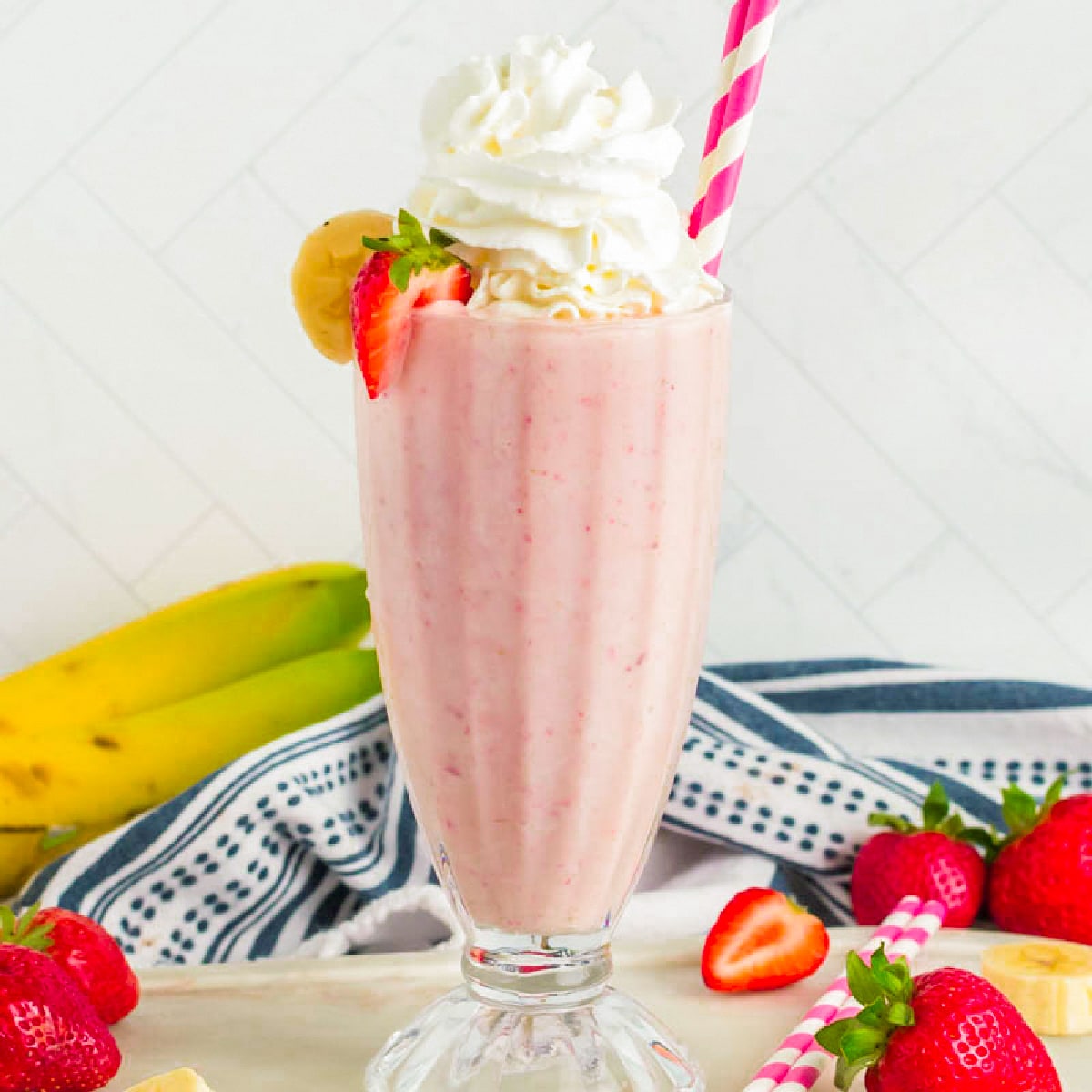 This Strawberry Banana Milkshake will bring back memories of childhood or create new memories for you to enjoy. Rich, creamy and full of fruit, this frozen treat is a delight. Milkshake in a glass topped with whipped cream and straw.