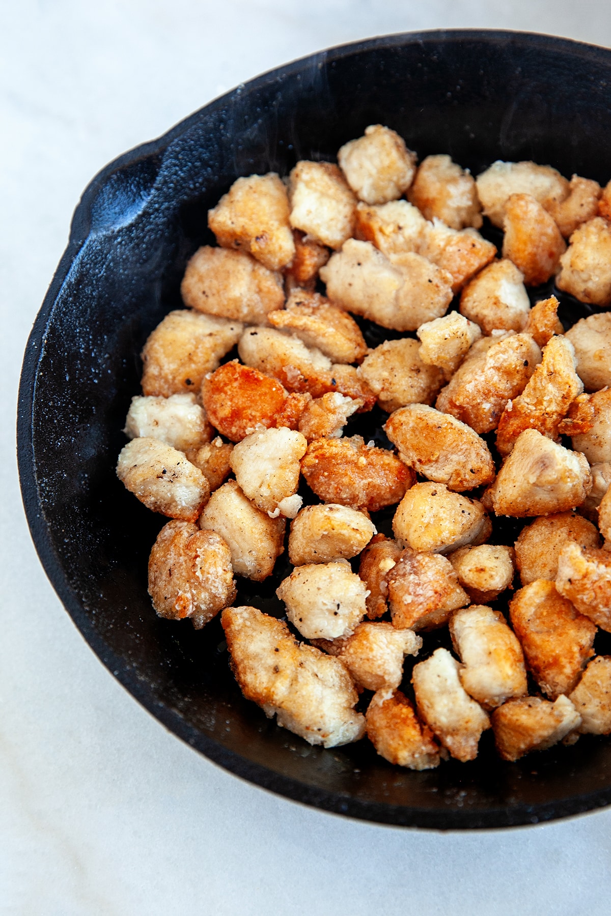 This Easy Orange Chicken Recipe will have you making this on repeat. It is way cheaper than takeout and completely free of MSG!! Frying up small cubes of chicken in cornstarch in a cast iron pan.