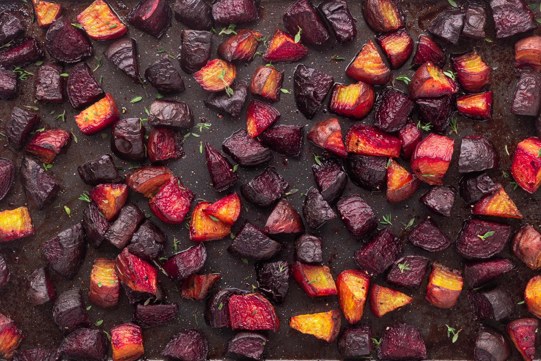Roasted Beets are an all-time favorite vegetable as they are easy to make and so delicious when cooked on high in the oven. Overhead of a panful of roasted beets with a sprinkle of thyme leaves.