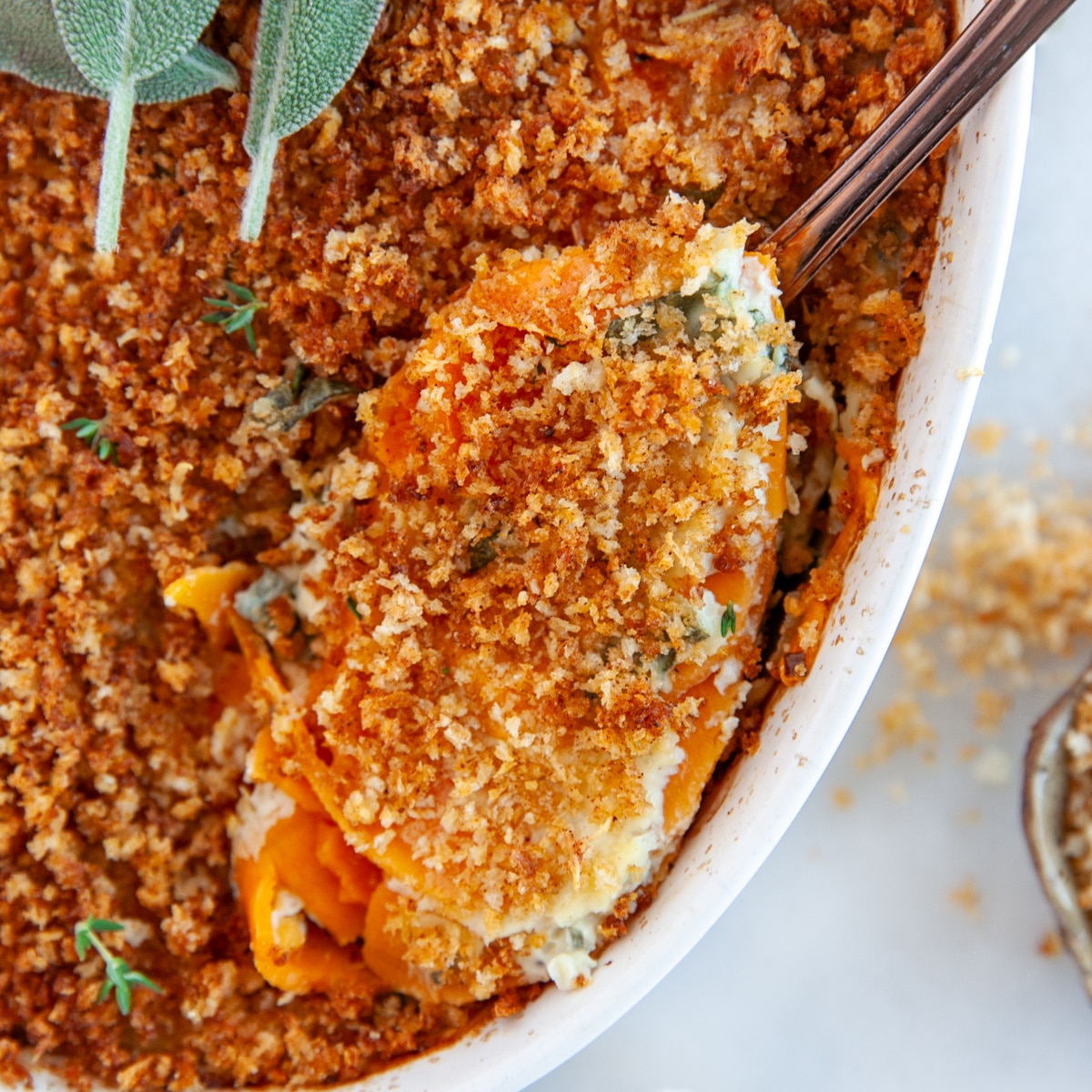 This Sweet Potato Au Gratin will be a hit with family and friends for the holidays. With a creamy herb and cheese flavored sauce and a crunchy savory topping - what is not to love!! Square photo of scooping out sweet potato au gratin.