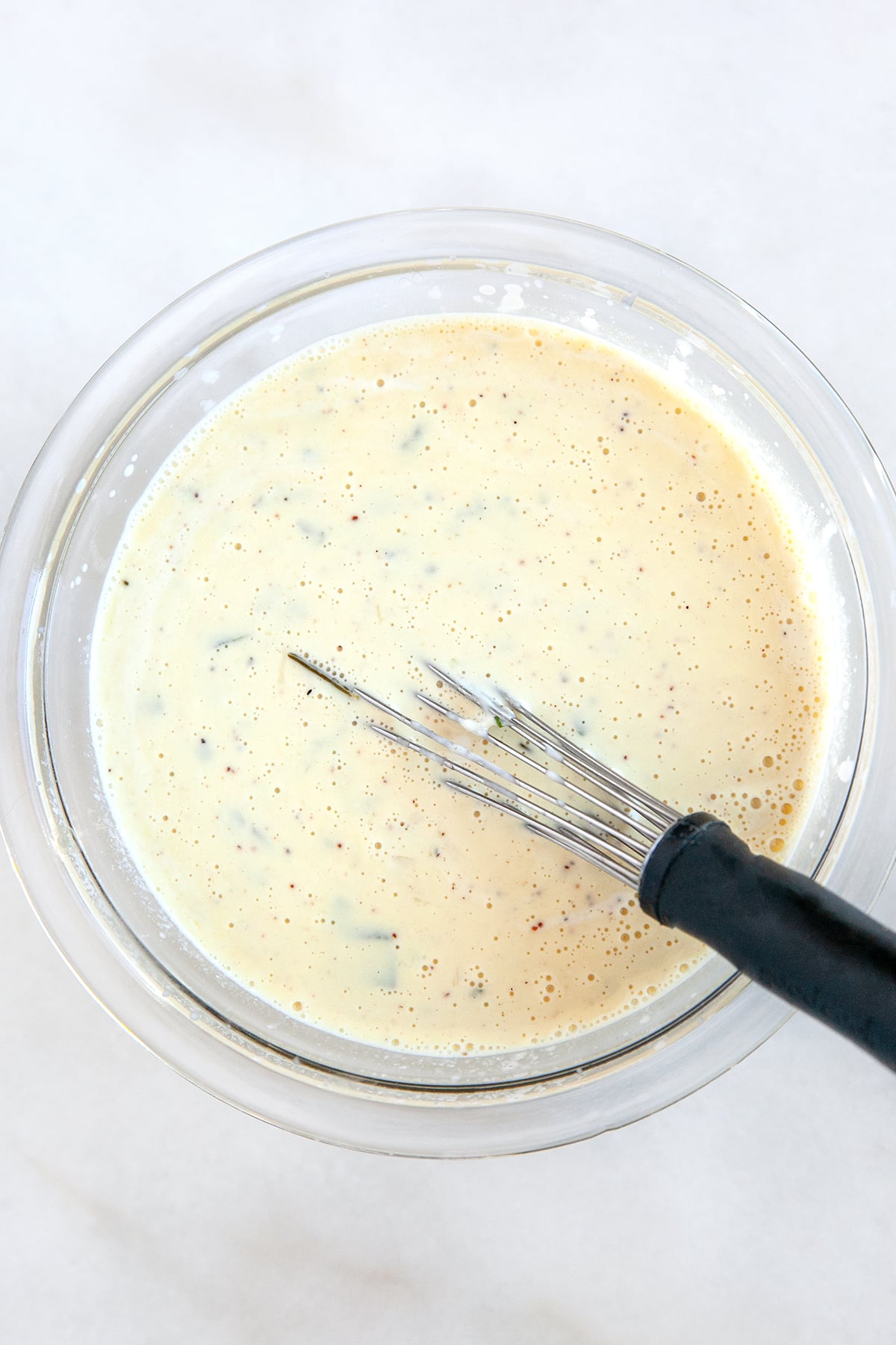This Sweet Potato Au Gratin will be a hit with family and friends for the holidays. With a creamy herb and cheese flavored sauce and a crunchy savory topping - what is not to love!! Cream sauce in a bowl with a whisk.