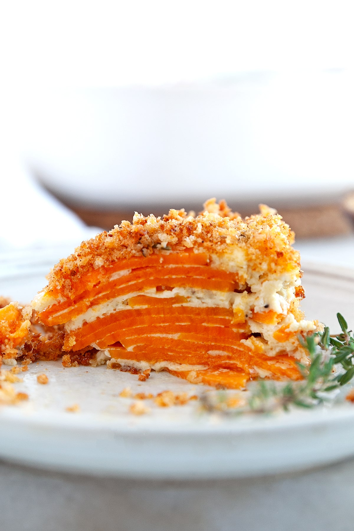 This Sweet Potato Au Gratin will be a hit with family and friends for the holidays. With a creamy herb and cheese flavored sauce and a crunchy savory topping - what is not to love!! Side view showing the layers of sweet potatoes in a slice.